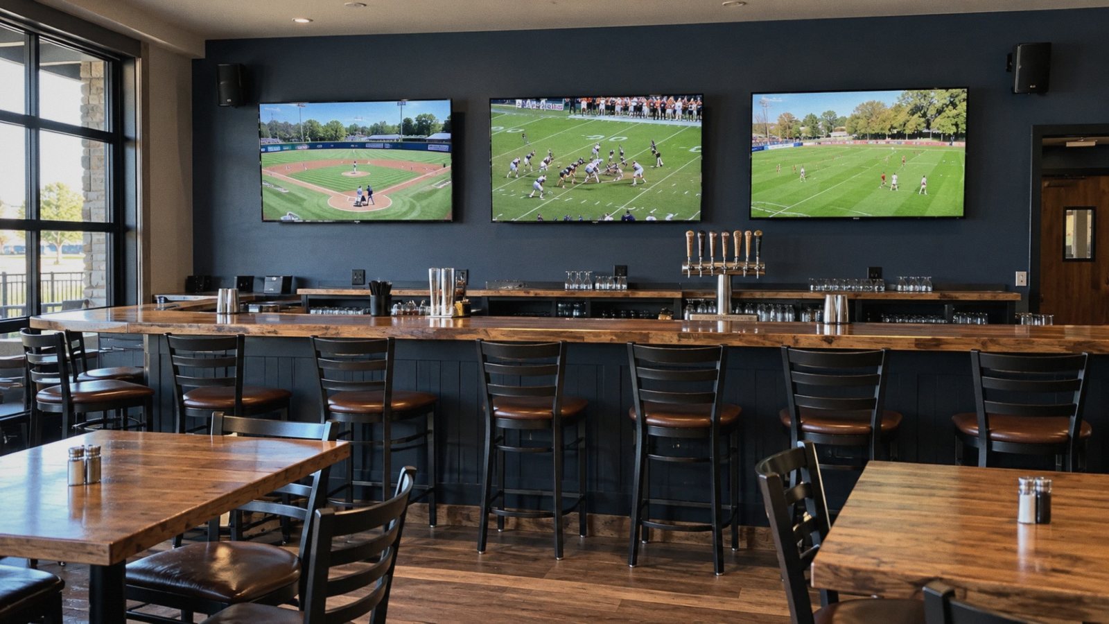 A bar with three TVs showing sports above the counter and speakers on the wall