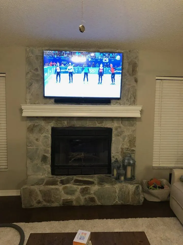 TV above a stone fireplace with a wood mantel