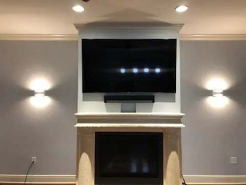 TV above a fireplace between two wall lights